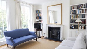 Un salon avec un canapé bleu, un canapé blanc, une cheminée et des étagères à livres.