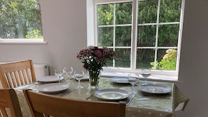 Een eettafel gedekt voor vier personen, met een bloemenvaas, borden en wijnglazen.