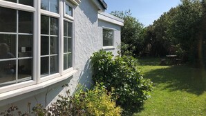 Een huis met grote ramen, een witte gevel en een verzorgde tuin met gazon en struiken.