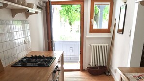 A kitchen with wooden flooring, a stove, cabinets, and a view through an open door to the outside. - Romantic, listed holiday apartment in Freiburg-Herdern on the church square (Nord)