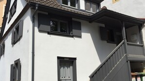A two-story building with a white facade, a dark staircase, and a small window with a curtain. - Romantic, listed holiday apartment in Freiburg-Herdern on the church square (Nord)