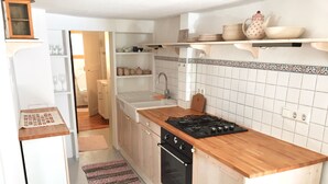 A kitchen with a wooden countertop, a stove, and white cabinets. There is a window above the sink and a door leading to another room. - Romantic, listed holiday apartment in Freiburg-Herdern on the church square (Nord)