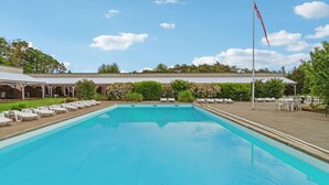 A rectangular swimming pool with a flagpole and lounge chairs around it.