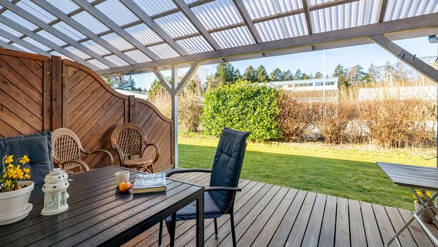 An outdoor patio with a wooden table, two chairs, and a potted plant.