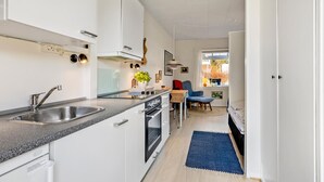 A modern kitchen with a built-in oven, a sink, and a dining area with a blue chair and a table.