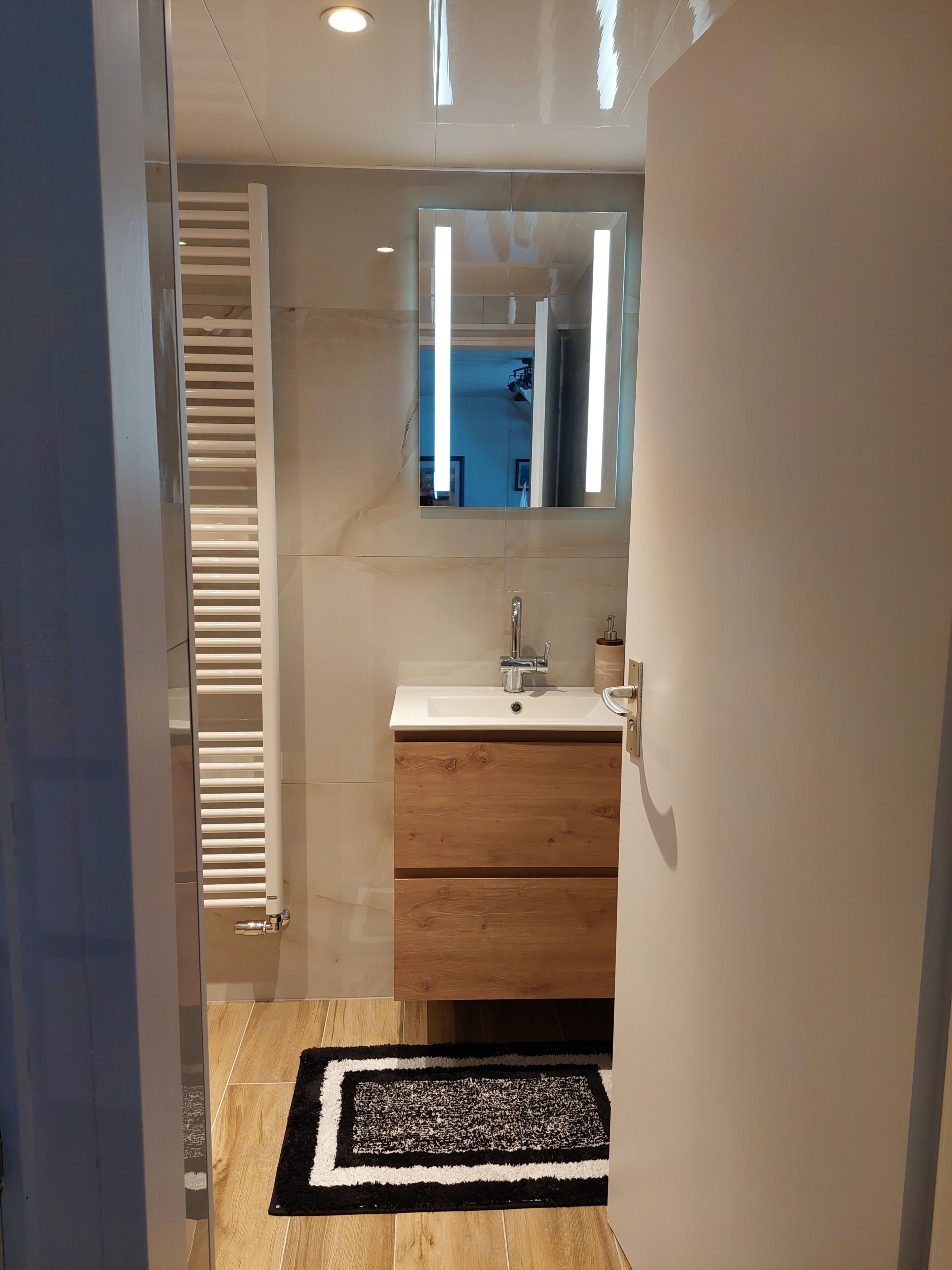 Ein Badezimmer mit einem weißen Waschbecken, einem Holzschranken, einem Spiegel und einem schwarz-weißen Teppich.