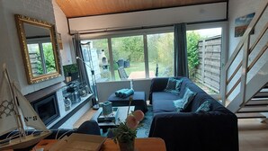 Un salon moderne avec un plafond en bois, une grande fenêtre, un canapé noir, une petite table avec une plante et un escalier.