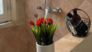 A bathroom with a white flower pot on a counter, a shower area, and a black basket with toiletries.
