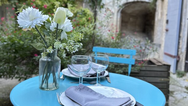 A table set with a vase of flowers, two wine glasses, and a folded napkin on a blue table.