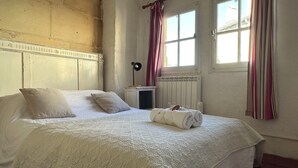 A bedroom with a large bed, a radiator, a nightstand, and a window with curtains.