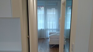 Een smalle gang met houten vloeren, witte muren, en een bed met wit beddengoed op de achtergrond.