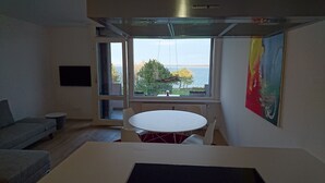 Een moderne kamer met een eettafel, een bank en een groot raam met uitzicht op zee.