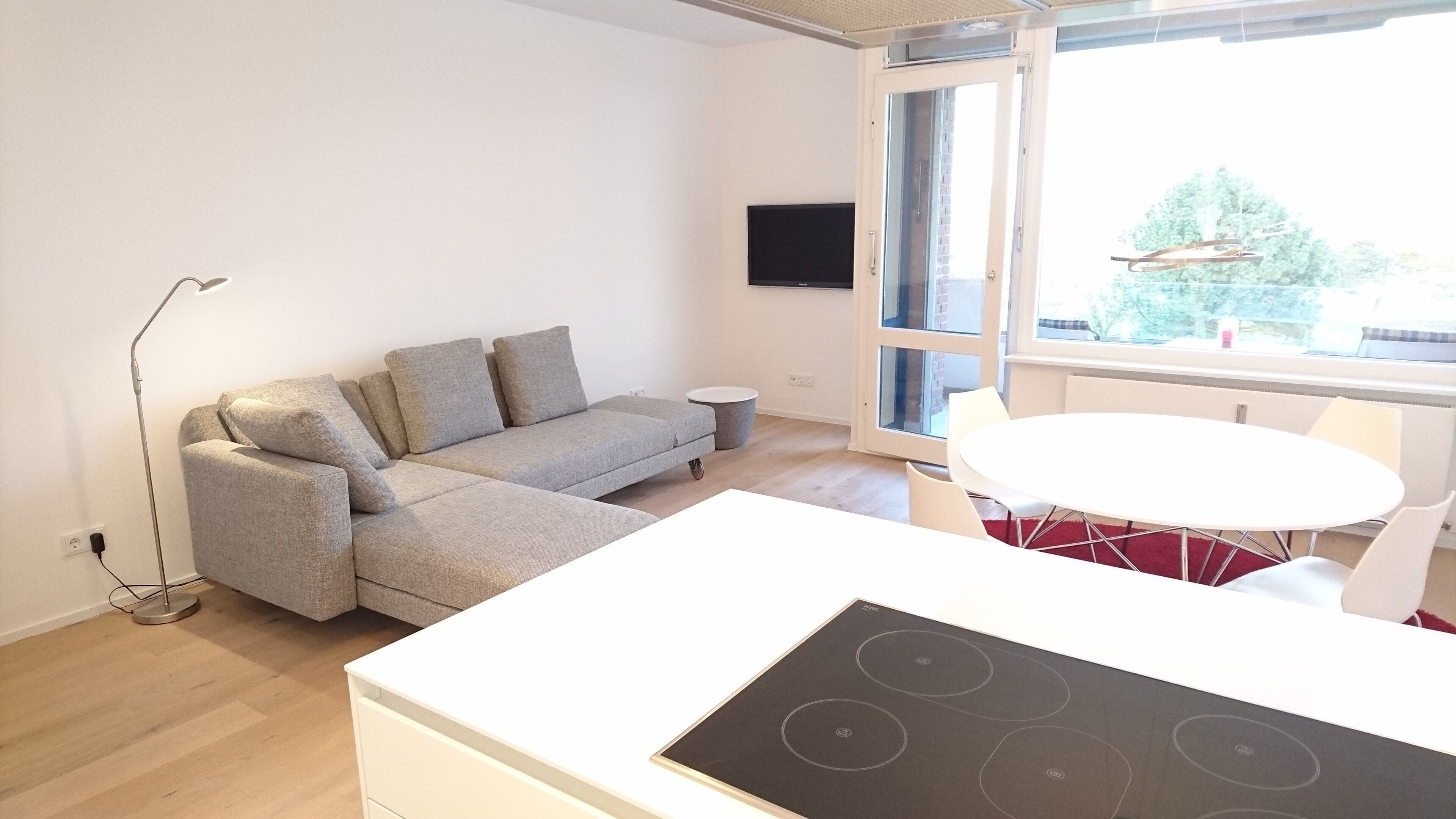 En moderne stue med en grå sofa, et lille rundt bord og et indbygget komfur.