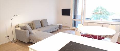 En moderne stue med en grå sofa, et lille rundt bord og et indbygget komfur.