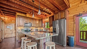 A wooden cabin kitchen with a large island, bar stools, stainless steel appliances, and a view through the door. - Ridge View Lodge • Nature/Mtn View • Hot tub • Firepit • Games • Parking 6 cars (Sevierville)