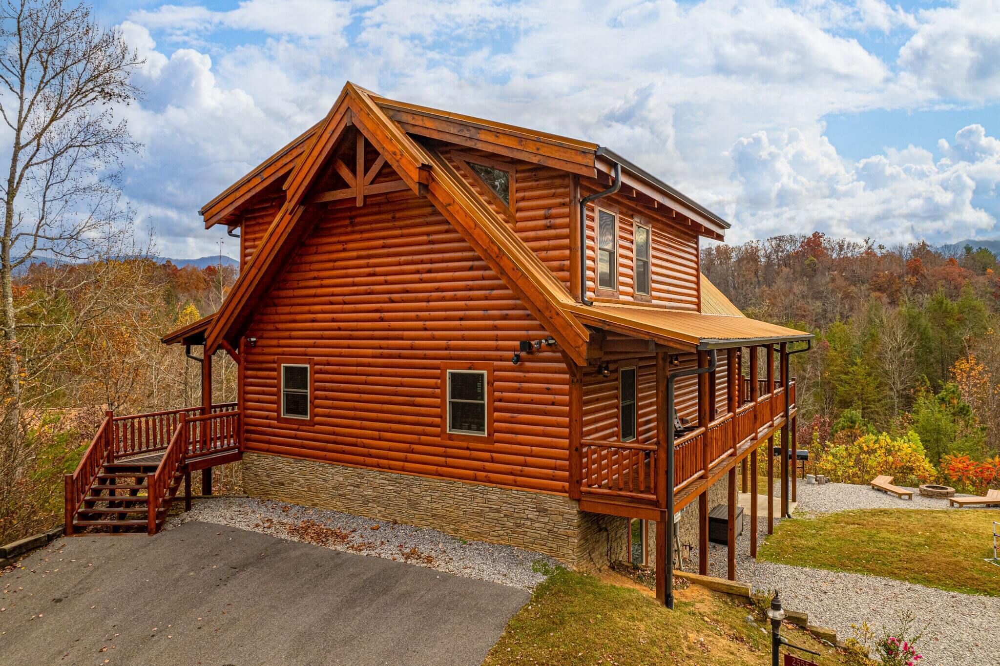 A log cabin with a balcony, a staircase, and a stone foundation.