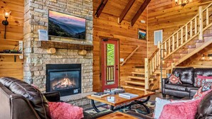 A cozy cabin interior with a fireplace, leather sofas, a wooden staircase, and a scenic view. - Ridge View Lodge • Nature/Mtn View • Hot tub • Firepit • Games • Parking 6 cars (Sevierville)