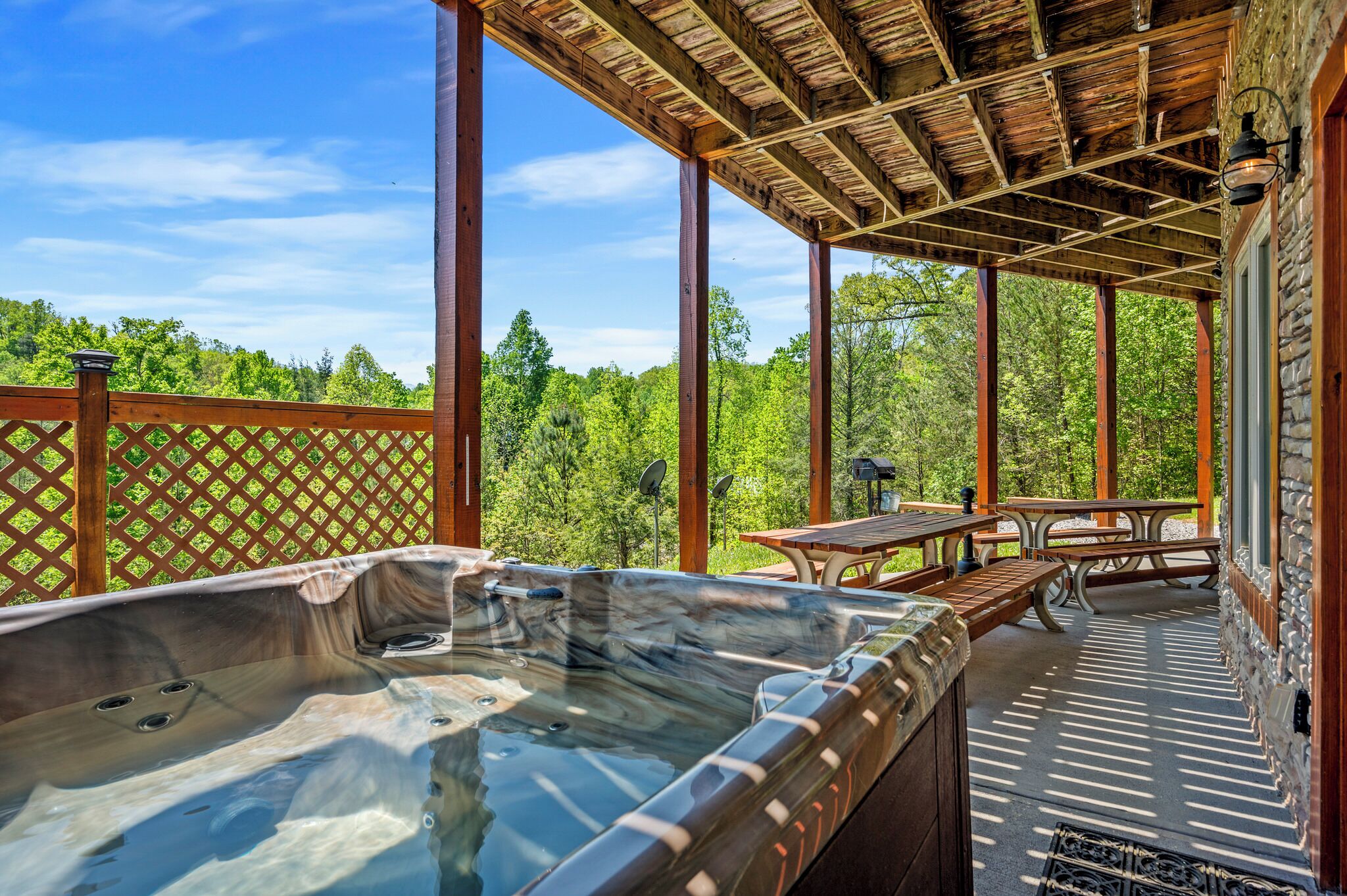 Een hottub op een overdekt terras met een houten pergola, omgeven door weelderig groen.