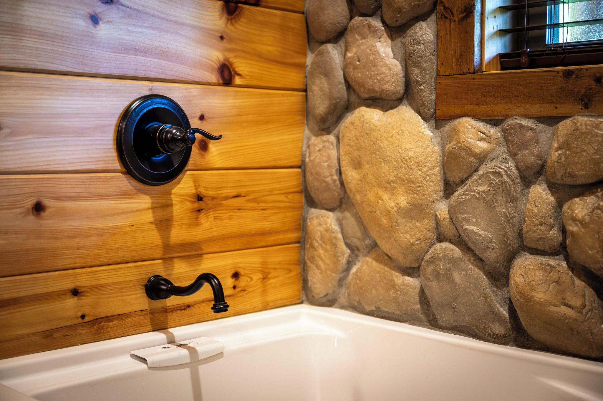 Ein Badezimmer mit einem Holzbadezimmerwaschbecken, einer Steinwand und einer weißen Badewanne.