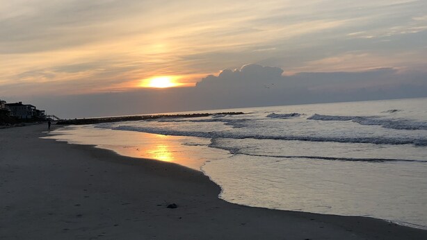 Una playa con un atardecer, olas y un muelle.