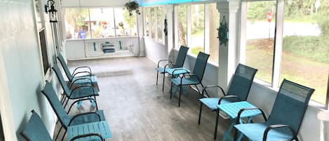Et overdækket udendørsområde med rækker af stole og borde, store vinduer og hængende ventilatorer.