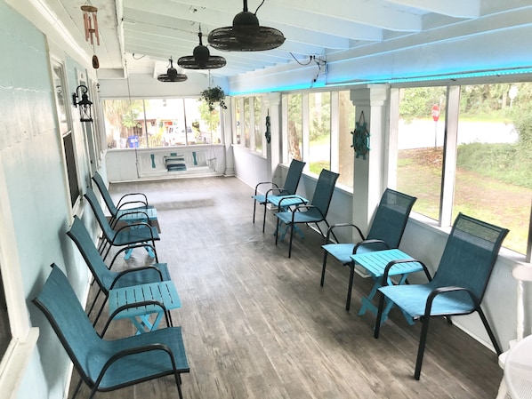 A covered outdoor seating area with rows of chairs and tables, large windows, and hanging fans.