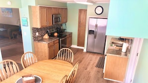 Una cocina con gabinetes de madera, un refrigerador de acero inoxidable y una zona de comedor con una mesa y sillas de madera.