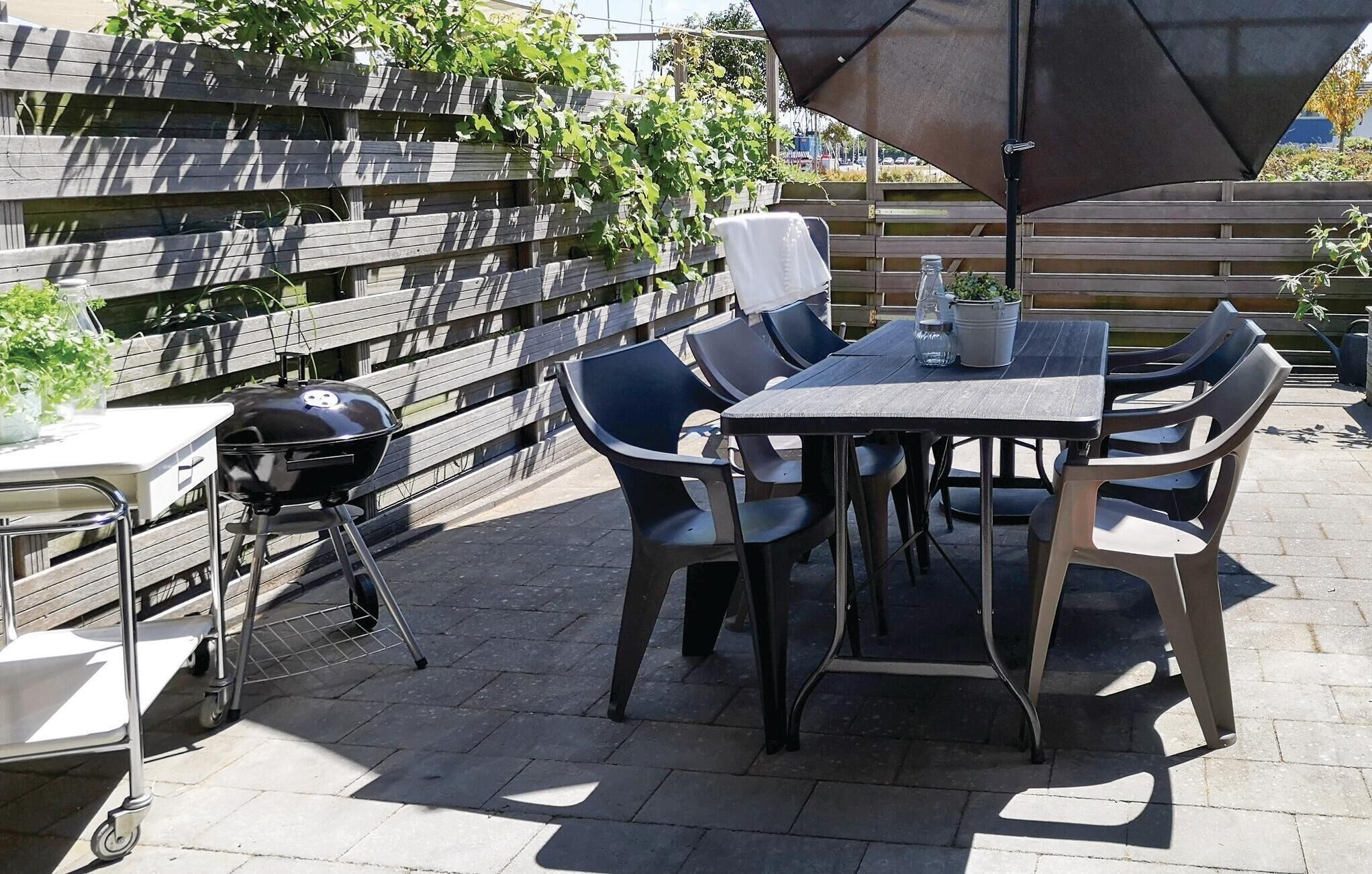 Un patio al aire libre con mesa y sillas, una parrilla y una sombrilla.