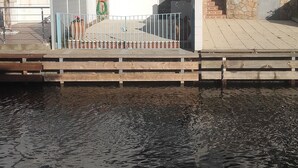 Ein Anwesen am Wasser mit einem weißen Gebäude, das einen Balkon, eine Holzsteg und einen klaren Blick auf das Wasser bietet.