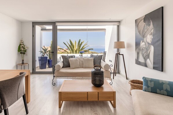 A modern living room with a wooden coffee table, a sofa, and a view of the sea through large windows.