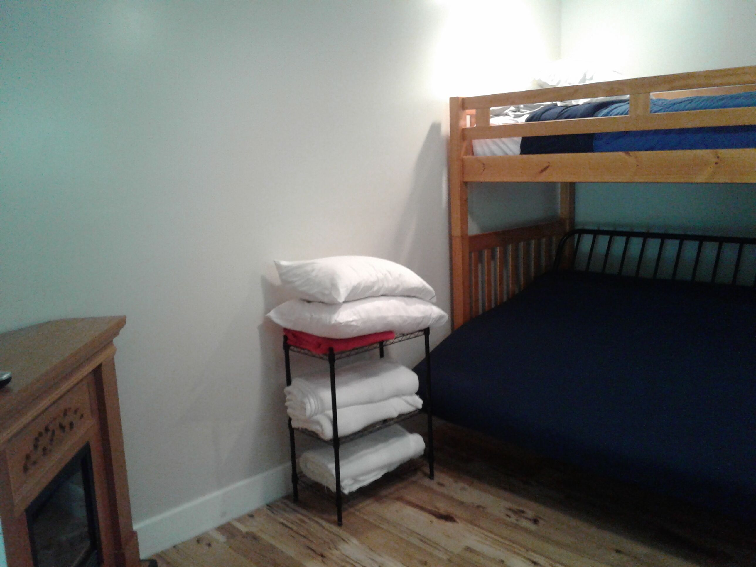 A room with a bunk bed, a wooden cabinet, and a shelf with folded towels.