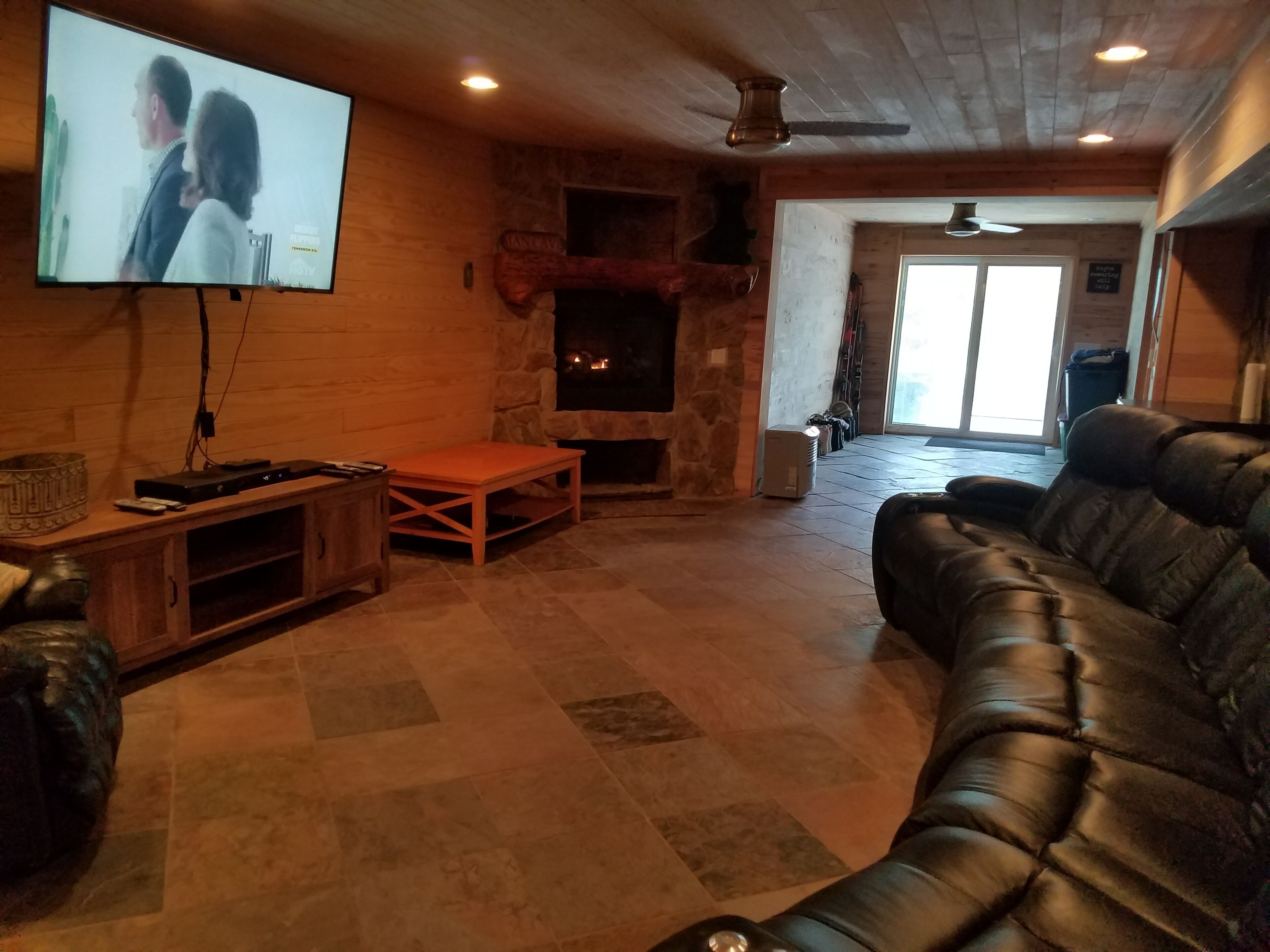 A cozy living room with a fireplace, leather sofa, and a flat-screen TV mounted on the wall.