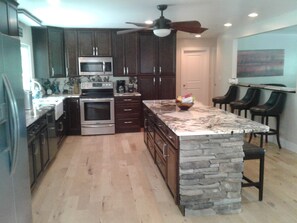 A kitchen with dark wood cabinets, a granite countertop, a stone island, a microwave, an oven, and a ceiling fan. - Ruskamp Retreat-SPACIOUS LUXURY LODGE, 5 MIN TO SLOPES, FIREPLACES, POOLTABLE (Banner Elk)