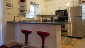 Een moderne keuken met witte kasten, roestvrijstalen apparatuur, een dubbele spoelbak en twee rode barkrukken.