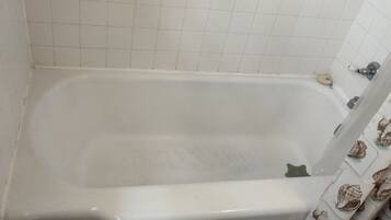 Una bañera con pared de azulejos blancos y cortina de ducha con estampado de conchas.