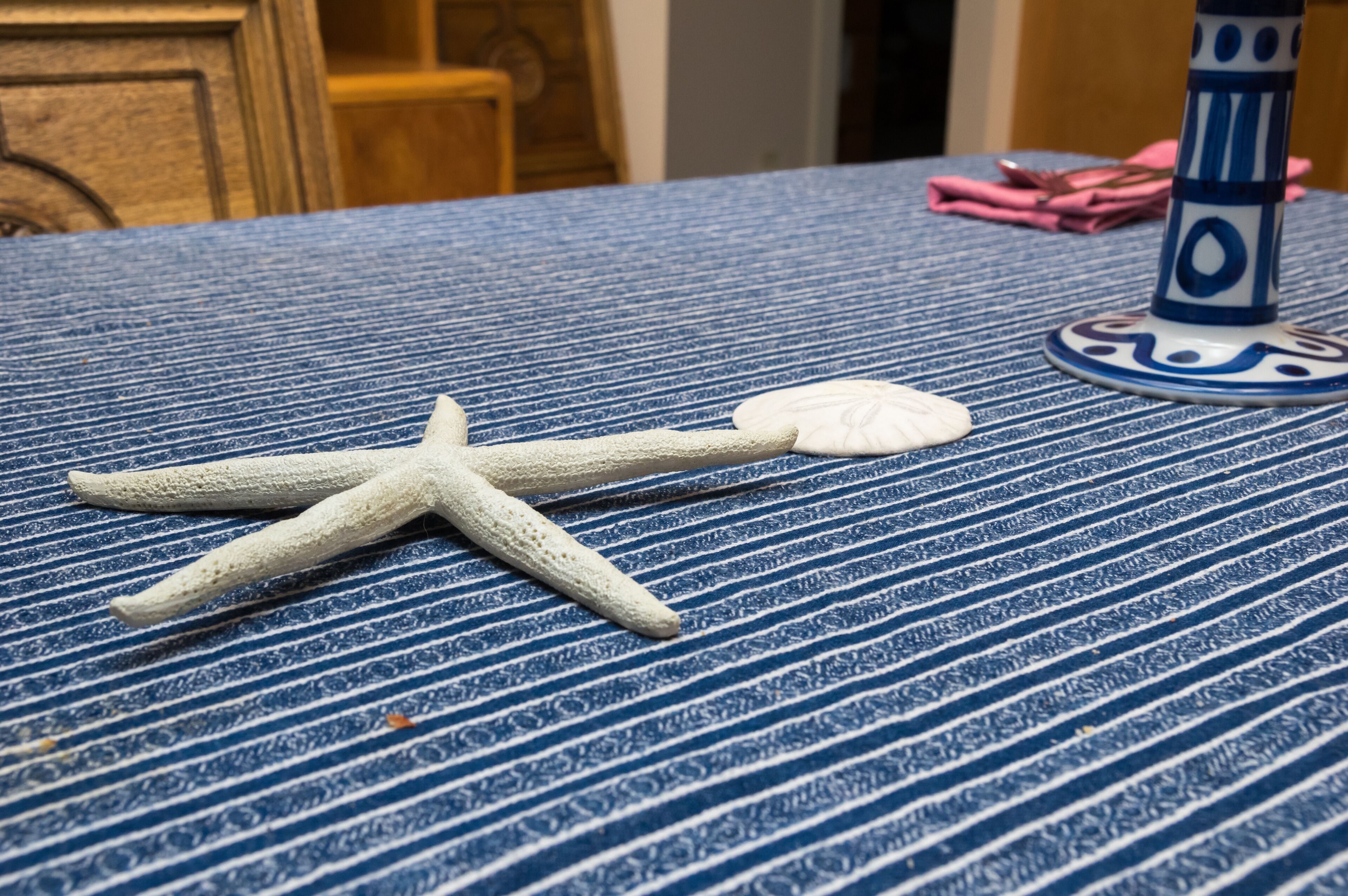 A table with a blue and white striped tablecloth, a white starfish, a white seashell, and a blue and white vase.