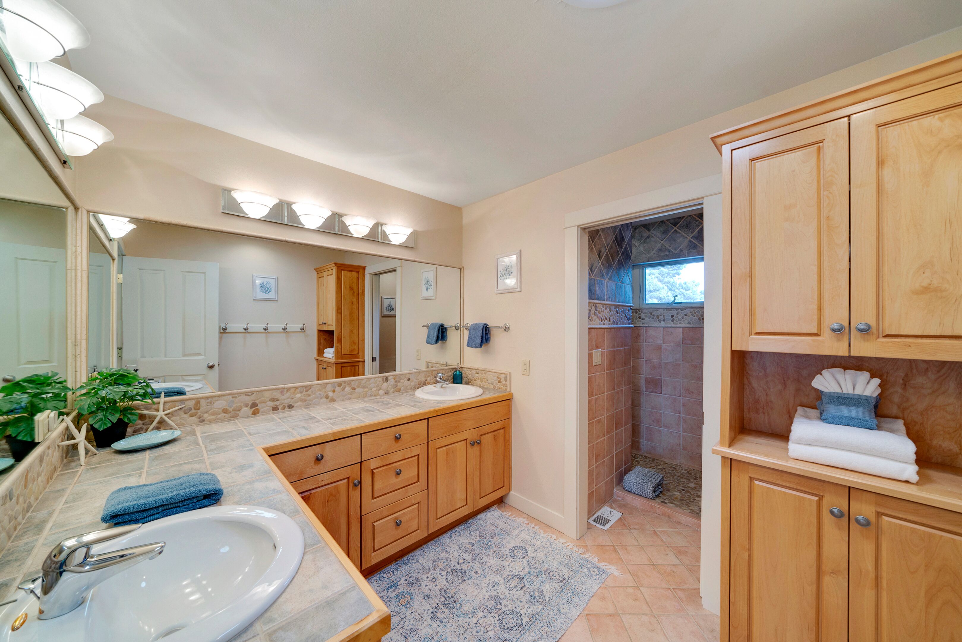 A bathroom with a sink, mirror, wooden cabinets, and a shower area.