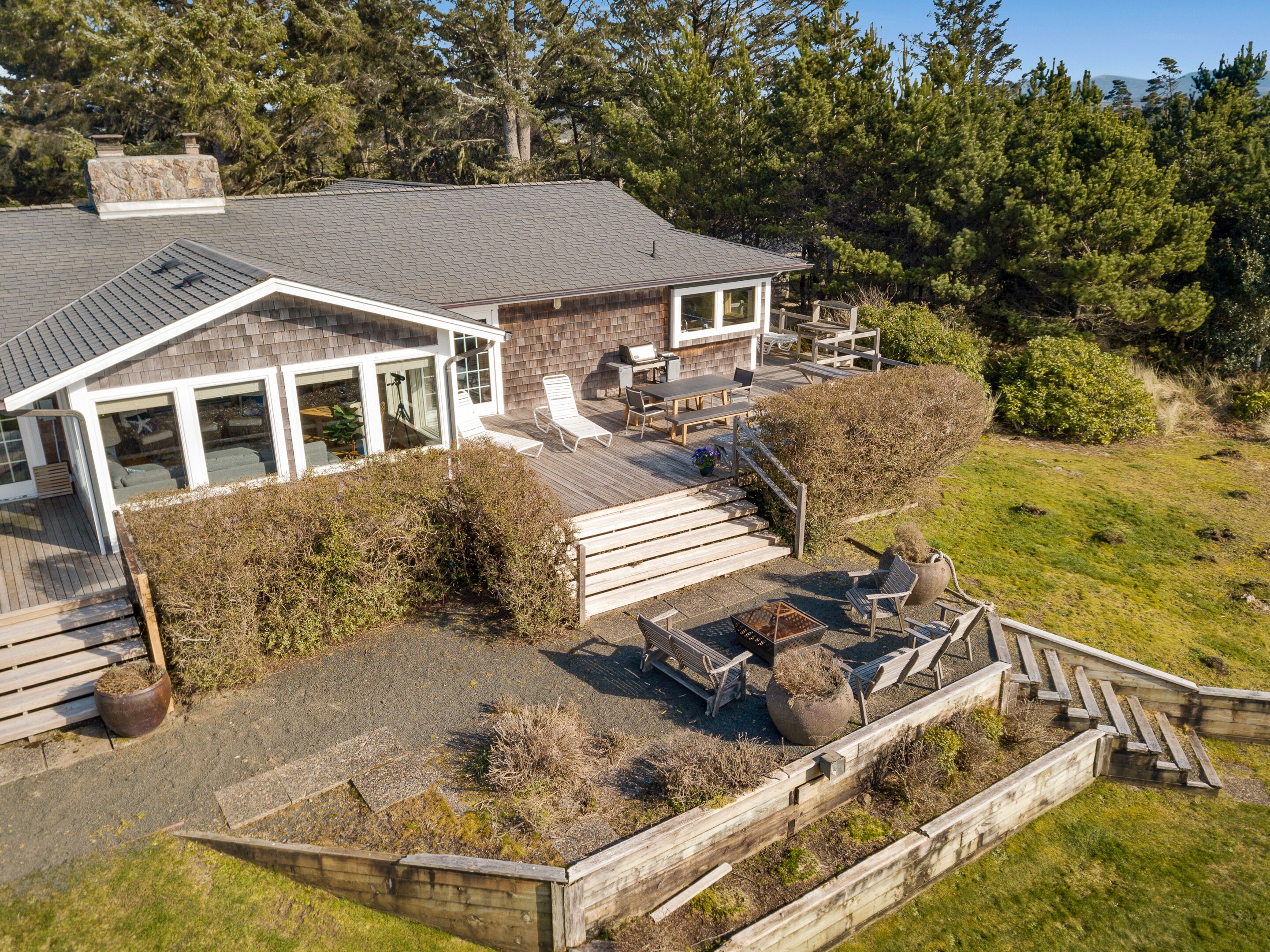 A modern house with a large deck, outdoor seating, and a stone fireplace.