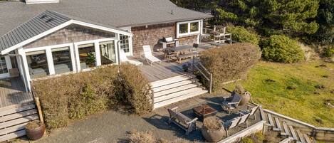 A modern house with a large deck, outdoor seating, and a stone fireplace.