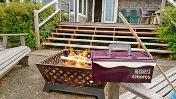 Een draagbare grill met een doos Hershey's S'mores er aan bevestigd, buiten geplaatst met houten banken en een huis op de achtergrond.