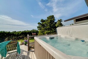Un jacuzzi en una terraza de madera con una vista despejada del cielo y árboles al fondo.