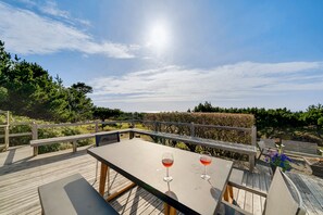 Una terraza de madera con dos copas de vino tinto, un banco y vistas al viñedo.