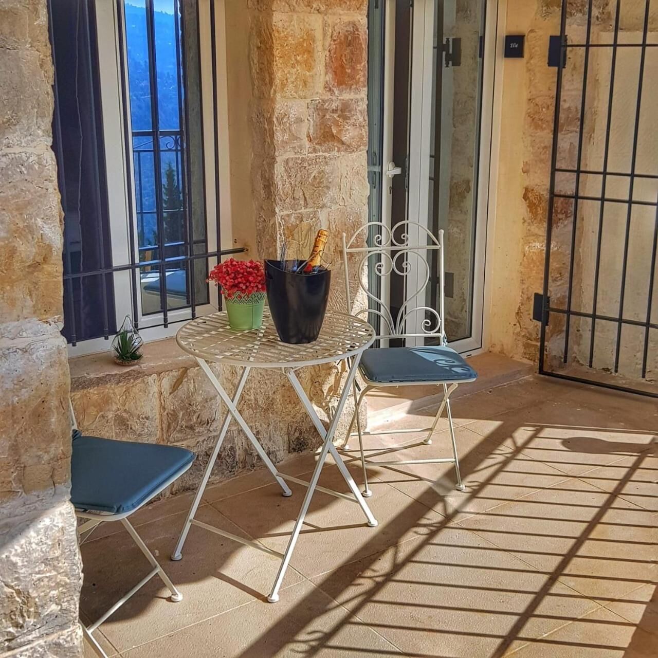 Un pequeño espacio al aire libre con una mesa y dos sillas, una planta en maceta y una botella de champán.