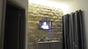 Une salle de bain avec un mur en pierre, un téléviseur fixé au mur, un meuble contenant des articles de toilette et un rideau de douche.