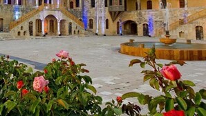A courtyard with a fountain, arches, and a staircase leading to an upper level. - Beit Lebbos (Beit Al Dine)