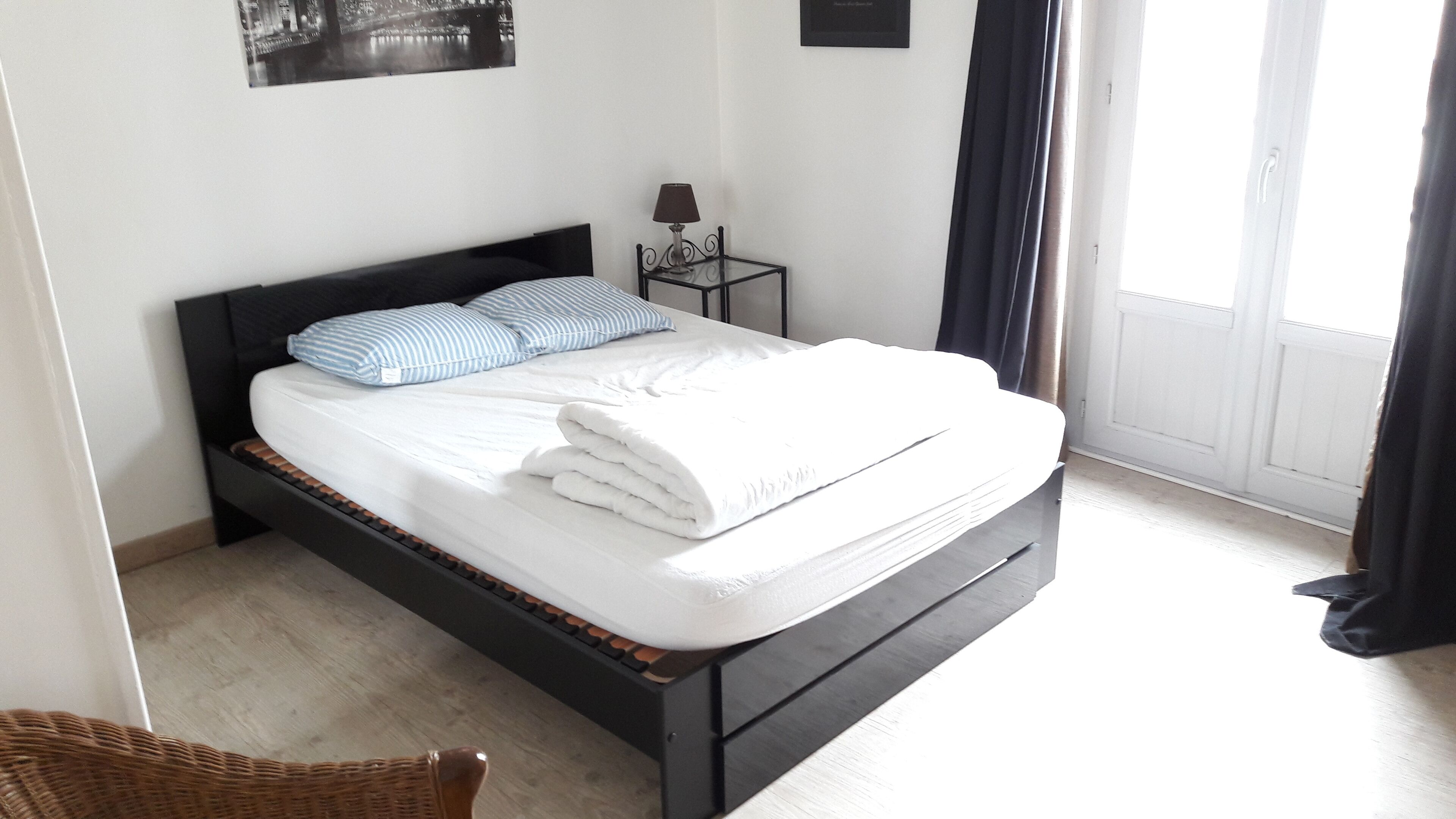 A neatly made bed with white linens and a folded blanket, a small bedside table with a lamp, and a framed picture on the wall.