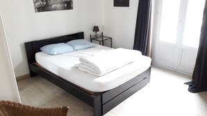 A neatly made bed with white linens and a folded blanket, a small bedside table with a lamp, and a framed picture on the wall.