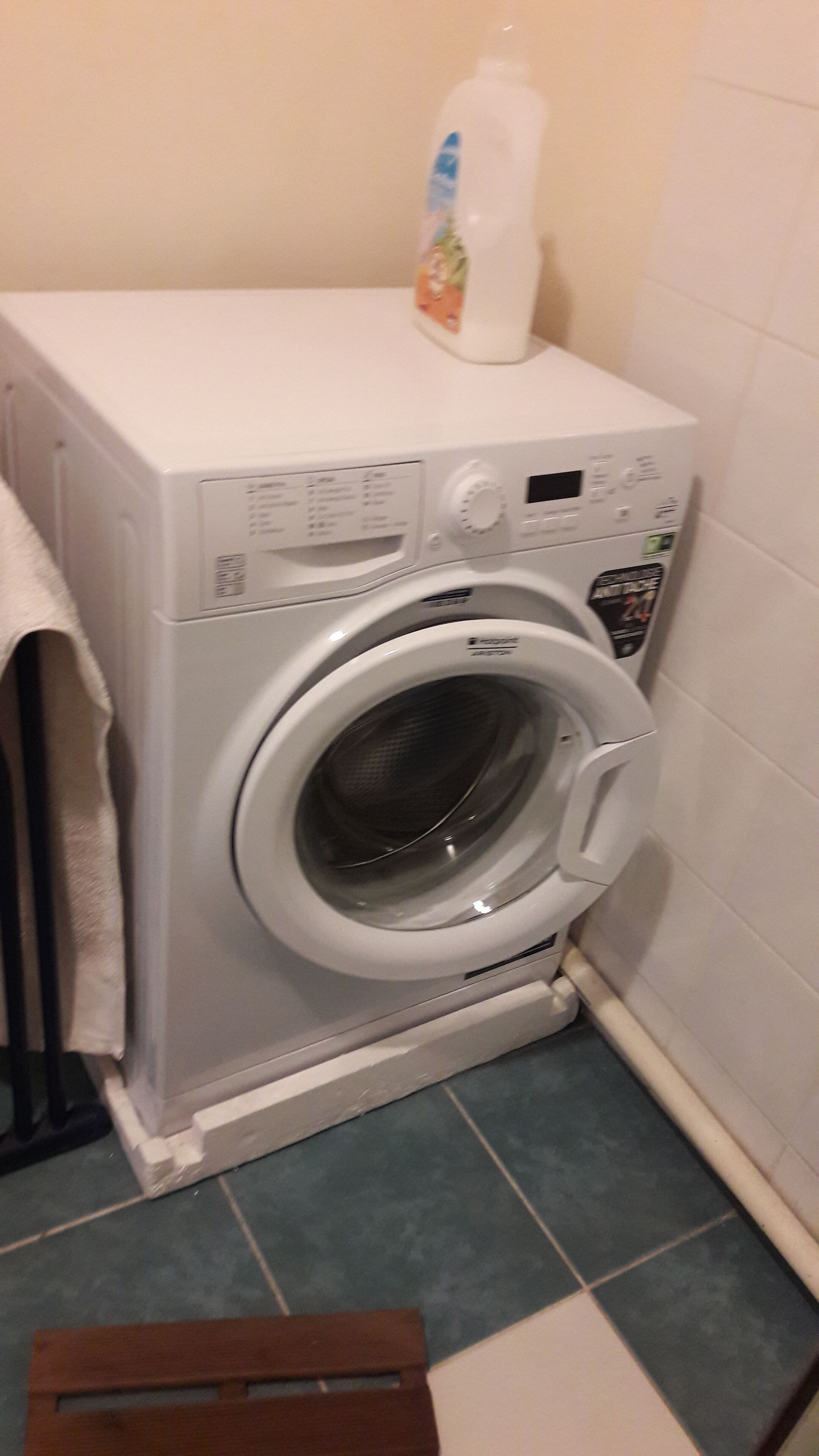 A front-loading washing machine in a small laundry room with a tiled floor and a white wall.