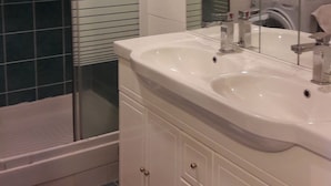 A bathroom with a glass shower enclosure, a white sink with a mirror, and a washing machine.