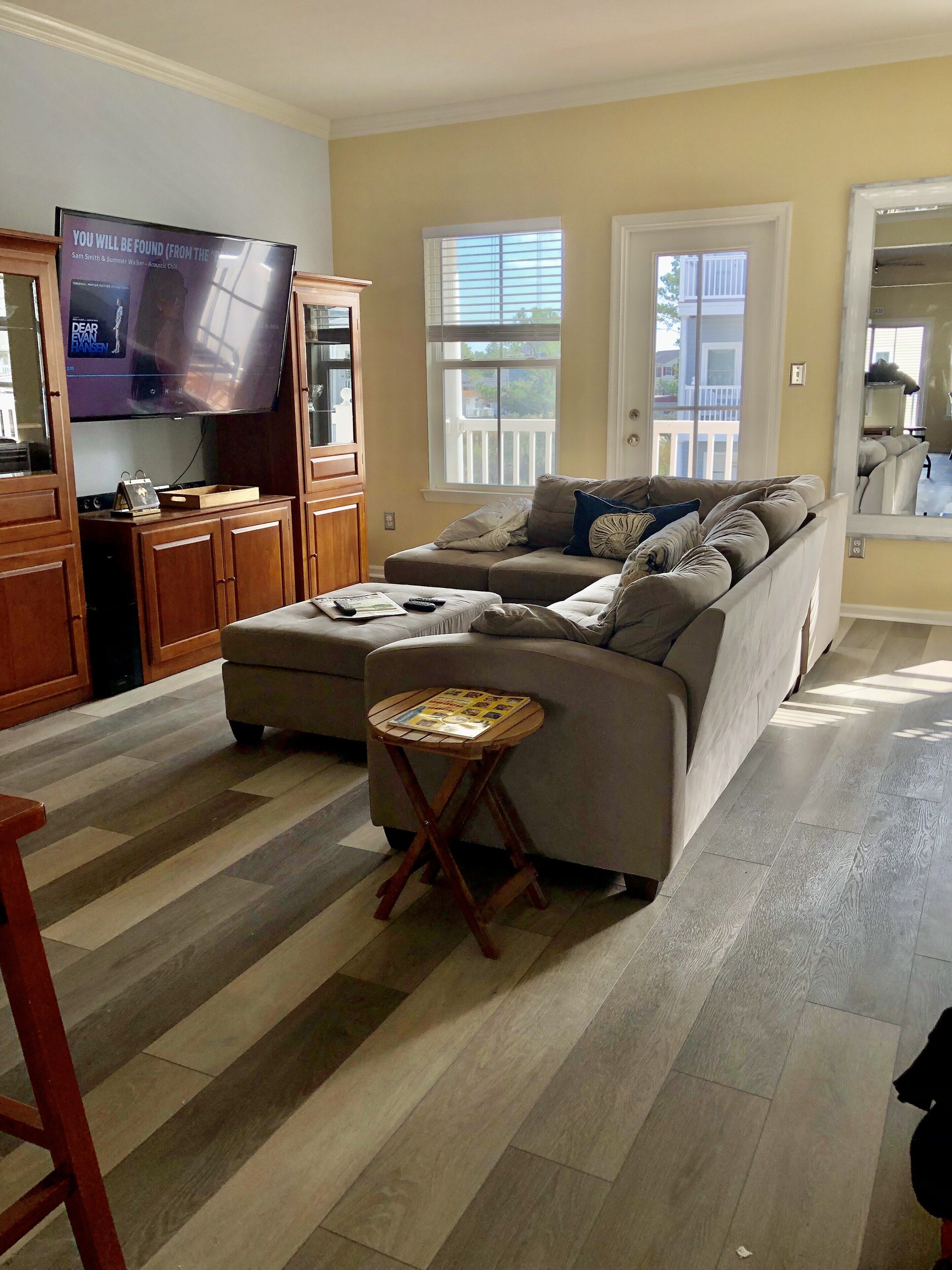 A living room with a sectional sofa, a small wooden table, a television, and a window with blinds.